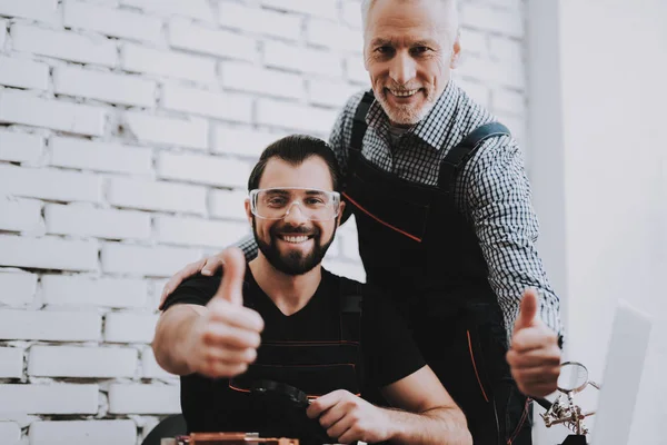 Two Exited Smiling Men in Uniform in Workshop. Repair Shop. Thumbs Up. Computer Hardware. Young and Old Workers. Modern Devices. Digital Device. Work in Workshop. Electronic Devices Concept.