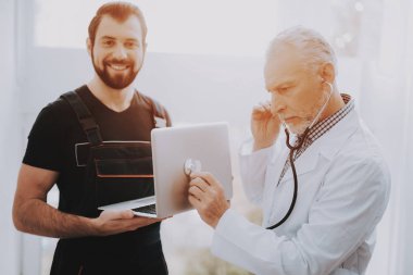 Bilgisayar Doktor stetoskop ile Beyaz üniformalı. Dizüstü bilgisayar ile genç adam. Didital aygıt incelenmesi. Modern cihazlar. Dijital aygıt. Elektronik cihazlar kavramı. Tanı Aracı.