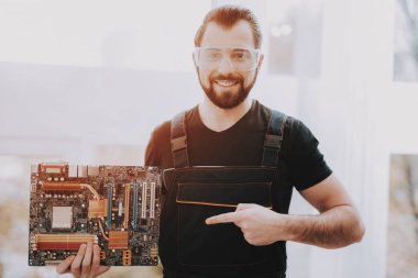 Genç işçi anakart ile el ayakta. Alt donanım ile. Modern atölye kavramı. Adam Modern aygıtları duran. Dijital aygıt. Elektronik cihazlar kavramı. Gözlüklü adam.