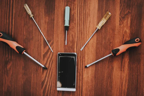 Telefone móvel quebrado com ferramentas na tabela de madeira . — Fotografia de Stock