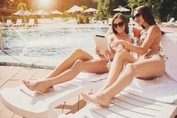 Dos hermosas mujeres acostadas usando la tableta cerca de la piscina . — Foto de Stock