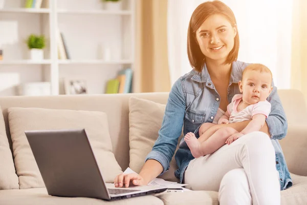 Glückliche Mutter benutzt tragbaren PC und hält Baby. — Stockfoto