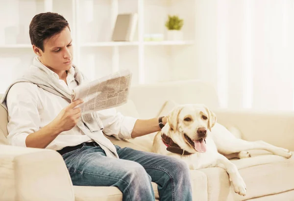 Giovane seduto sul divano bianco con cane a casa . — Foto Stock