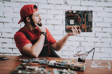 Atölye kırık anakartlar genç adam kırmızı şapkalı. Modern atölye kavramı. Üretim aracı. Modern araçları kavramı. Elektronik cihazlar kavramı. Mobil aygıt donanım. Ahşap Resepsiyon.