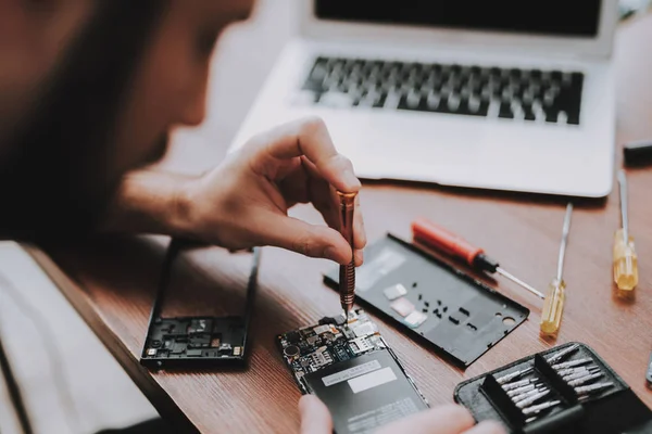 Yakın çekim. Cep telefonu tamir genç adam. Dükkanı onarın. Araçları ile çalışan. Büyüteç Camı. Dijital aygıt. Araçları üstünde okul sırası. Elektronik cihazlar kavramı. Hareket eden aygıt. Smartphone onarım.
