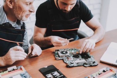 İki adam Pc. onarım donanım ekipmanları tamir dükkanı. Araçları ile çalışan. Bilgisayar donanım. Genç ve yaşlı işçi. Modern cihazlar. Dijital aygıt. Laptop üstünde okul sırası. Elektronik cihazlar kavramı.