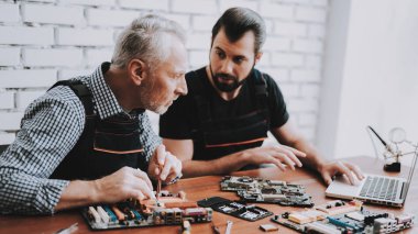 İki adam Pc. onarım donanım ekipmanları tamir dükkanı. Araçları ile çalışan. Bilgisayar donanım. Genç ve yaşlı işçi. Modern cihazlar. Dijital aygıt. Laptop üstünde okul sırası. Elektronik cihazlar kavramı.
