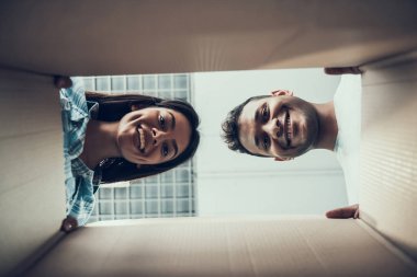 Genç çift Caton kutusu içinde gülümseyen. Alt görünümü güzel çiftin karton kutunun içini arıyor. Genç çift yeni daire/açma karton kutular tadını çıkarın. Kavram yerini değiştirme
