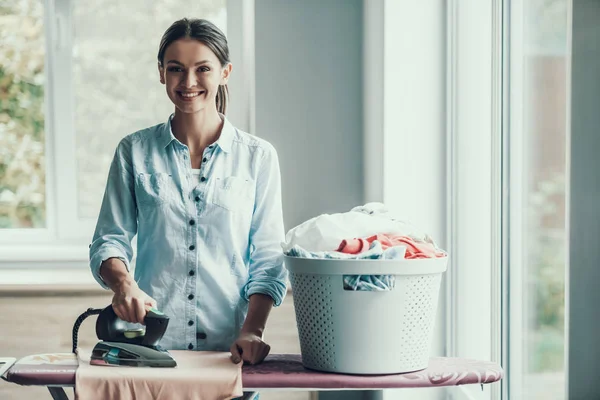 Young Smiling Woman Ironing Clothes after Laundry. Happy Beautiful Girl enjoying Ironing Clean and Fresh Clothing just after Laundry. Young Attractive Woman doing Housework. House laundry