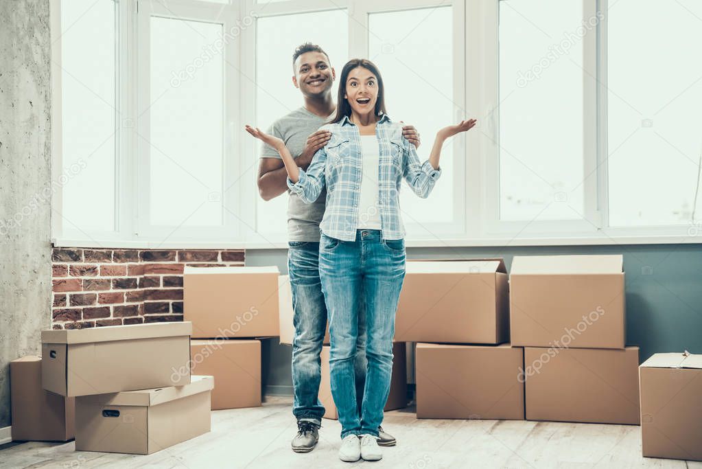 Young Smiling Couple Enjoy Moving in New House. Young Beautiful Couple Hugging with Stack of Cardboard Boxes on Background in empty Apartment. Relocation and House Moving Concept