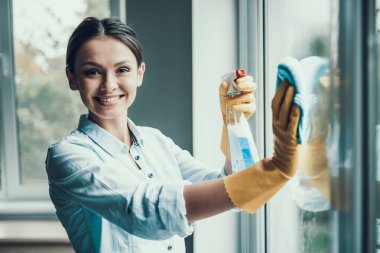 Genç kadın yıkama pencere sünger ile gülümseyen. Mutlu güzel kız ilaçlama temizlik ürünleri ve sünger ile silerek tarafından koruyucu eldiven pencere temizleme giyiyor. Kadın ev temizliği