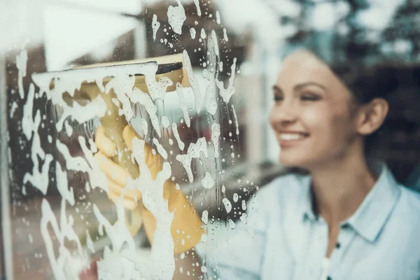 Young Smiling Woman Washing Window with Sponge. Happy Beautiful Girl wearing Protective Gloves Cleaning Window by spraying Cleaning Products and wiping with Sponge. Woman Cleaning House