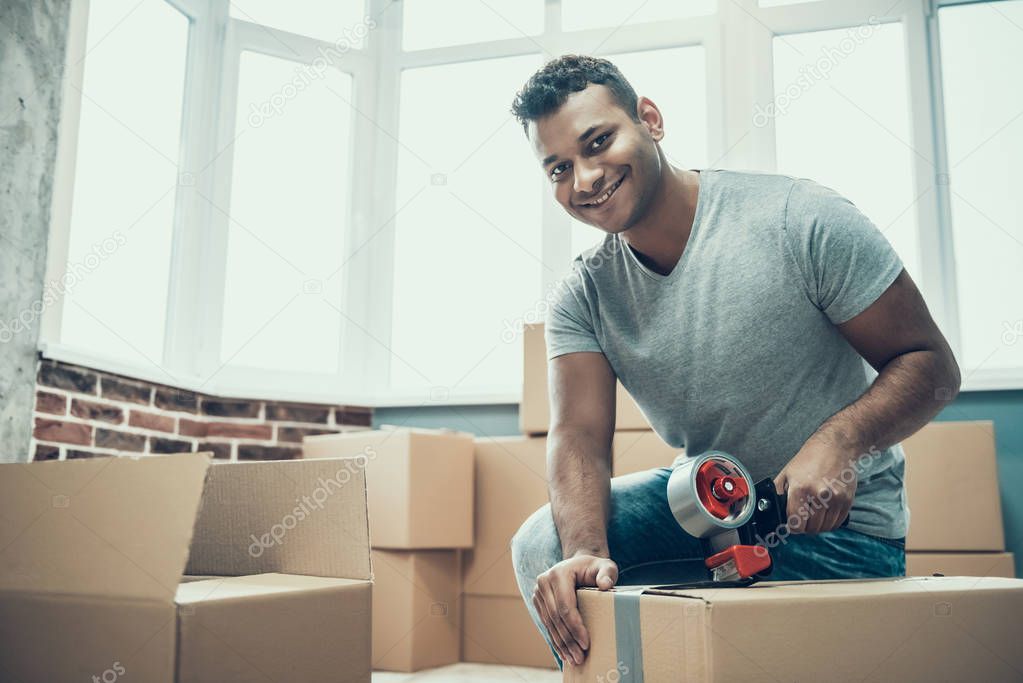 Young Smiling Man Packing Cardboard Box at Home. Happy Handsome Guy Preparing to Relocation by Packing Carton Boxes with Scotch Tape. Young Guy Moving to new Apartment