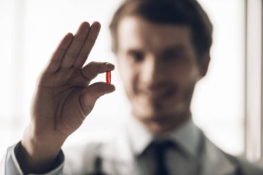 Genç Gülümseyen Doktor 'un Kırmızı İlacı Tutması' nın yakın çekimi. Erkek El Tutma Kırmızı hapına yaklaş. Sağlık ve Tıp Konsepti. Doktor beyaz önlük giyip, Pencere kenarındaki hastanede ilaç kullanıyor.