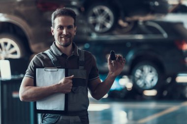 Otomatik mekanik Pano ve araba anahtarları tutan. Onarım Servisi. Yakışıklı ciddi beyaz adam siyah araba önünde gri Tekdüzen duran ve garajda çalışan servis siparişinin bitmiş sağlık kontrolü