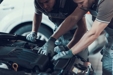 Araba tamiri yaparken iki tamircinin yakın çekimi. Üniformalı ve Eldivenli Güçlü Kaslı İşçiler Otomobil Motorunu Ciddi İfadeyle Açık Başlıklı Pozisyonuyla Tamir Ediyor. Onarım Servisi Konsepti