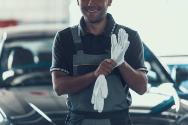 Otomatik mekanik garajda beyaz eldivenler. Yakın çekim yakışıklı ciddi beyaz Tamirci arabanın önünde duran gri üniformalı. Onarım hizmet anlayışı. Otomobil ana kavram