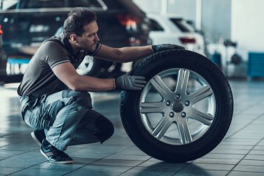 Beyaz yakışıklı otomatik mekanik Cheking araba tekerleği. Yetişkin makinist giyen üniforma iş garajda yapıyor portresi. Teknik meslek. Otomobil tamir hizmeti kavramı.