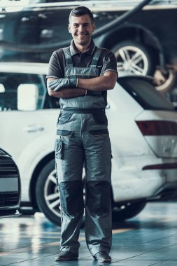 Yakışıklı gülümseyen araba tamircisi garajda duruyor. Portre otomobil önünde çapraz kolları olan karanlık üniformalı Kafkas yetişkin teknisyen ustası. Araba hizmet anlayışı onarma