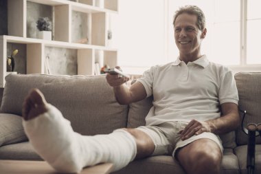 Kırık Bacaklı Adam Kanepeye Oturun ve Tv İzle. Rehabilitasyon ve Sağlık Kavramı