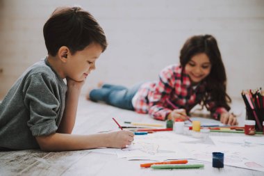 Sevimli Kardeşler Yerde Yerde Yatan İşaretlerle Çizim Yapıyor. Kafkas Çocuk ve GIrl, Beyaz Tahta Zemin 'de Günlük Giysiler Giyiyorlar Renkli Kalemler, Kağıt, Sabit Kullanıyorlar. Yaratıcı Çocuklar Konsepti