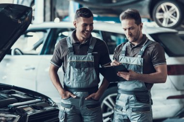 Garajda iki tane yakışıklı tamirci var. Gri Üniformalı Çekici Tamircilerin Portresi Olumlu Duyguları Gösteriyor Araba Kontrol Formu Teftişten sonra dolduruyor. Onarım Servisi Konsepti.