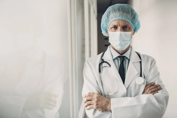 Serious Doctor in Mask and Cap with Crossed Arms. Medicine Worker Standing in Hospital with Stethoscope on Neck Wearing Lab Coat Posing with Crossed Arms Looking at Camera. Healthcare Concept