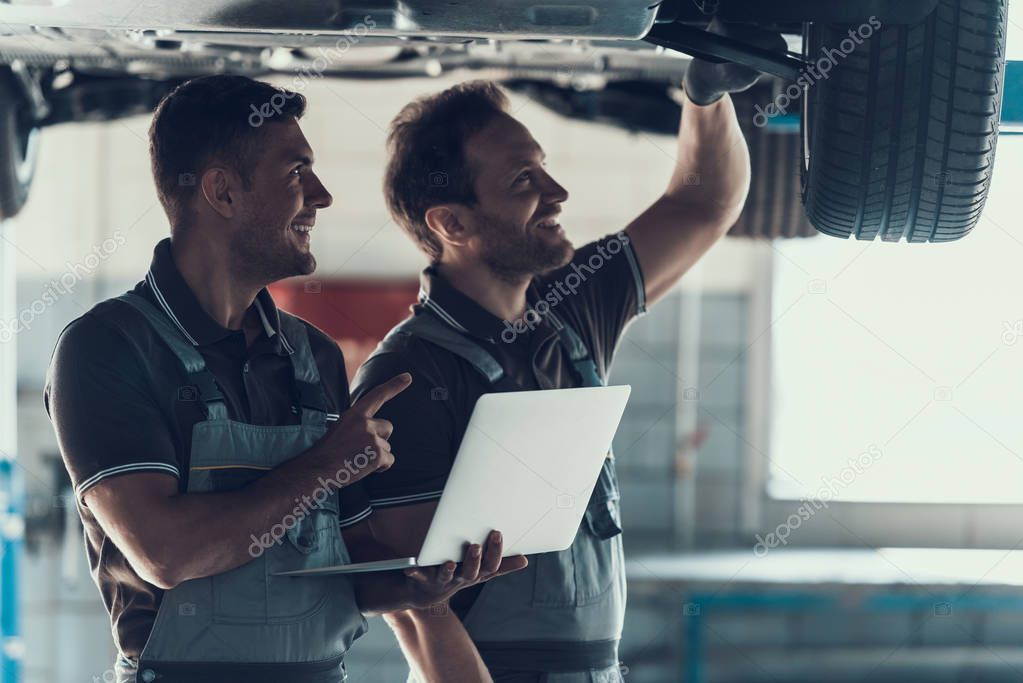 Mechanics Checking Wheel Bearings in Car Workshop. Two Caucasian Adult Technician Master in Uniform Repairing Car. Repairman Looking at Car Using Laptop. Auto Service Concept
