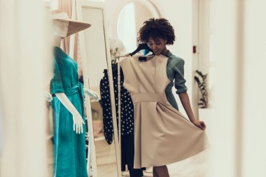 Giyim Mağazasında Gülümseyen Genç Kadın Alışveriş. Mutlu Güzel Siyah Kız Mall içinde Butik Satın Almak için Elbise seçerek. Giyim Mağazası'nda Afro saç modeli ile Çekici Afrikalı Kadın