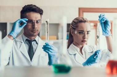 Genç bilim adamları Laboratuvar'da Sampes'e bakıyorlar. Beyaz Önlük Giyen Araştırmacılar Eldiven ve Koruyucu Gözlük Flasks Kimyasal Sıvı Örnekleri inceleyerek. Laboratuvarda Bilim Adamları Çalışıyor