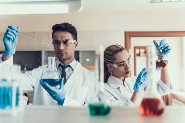 Genç bilim adamları Laboratuvar'da Sampes'e bakıyorlar. Beyaz Önlük Giyen Araştırmacılar Eldiven ve Koruyucu Gözlük Flasks Kimyasal Sıvı Örnekleri inceleyerek. Laboratuvarda Bilim Adamları Çalışıyor