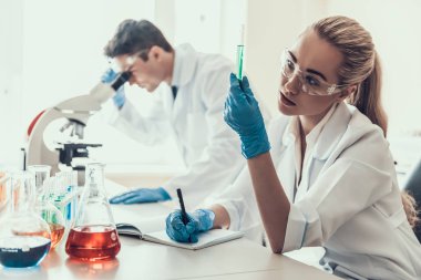Laboratuvarda Örnekleri Inceleyen Genç Bilim Adamları. Kadın Araştırmacı, Mikroskop kullanan Erkek Bilim Adamı iken Flasks Kimyasal Sıvı Örnekleri bakıyor. Laboratuvarda Bilim Adamları Çalışıyor