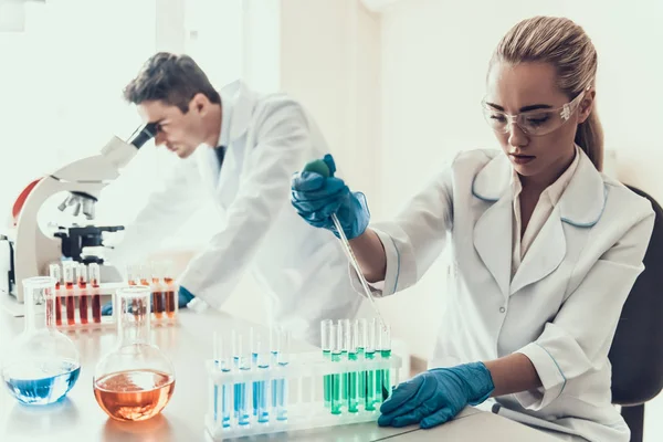 Laboratuvarda Örnekleri Inceleyen Genç Bilim Adamları. Kadın Araştırmacı, Mikroskop kullanan Erkek Bilim Adamı iken Flasks Kimyasal Sıvı Örnekleri bakıyor. Laboratuvarda Bilim Adamları Çalışıyor