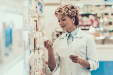 Eczanede ilaç şişesi olan eczacı. Yetişkin kadın eczacının portresi beyaz önlüklü ayakta dikilen ve eczanede hapları tutan. Eczanede çalışan eczacı.