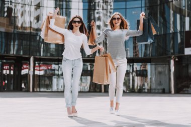 Alışveriş Çantalı Genç Kadınlar Şehir Caddesinde yürüyor. Satış, Tüketim ve İnsanlar Konsepti. Alışveriş ve Turizm Konsepti. Sunny Day 'de Alışveriş yaptıktan sonra Sokakta Yürüyen Kızlar Torbası.