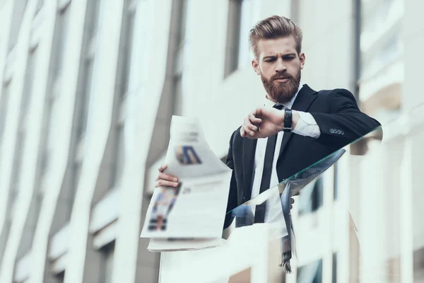 Serious Businessman Reading Newspaper Outdoor. Man Waiting Somebody. Bearded Serious Man Wearing Suit and Glasses, Standing Outdoor and Reading Newspaper. Business Concept.