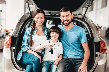Aile yeni bir arabanın bagajında oturuyor. Gülümseyen müşteriler. Bir galeride satın alma. Otomobil Salon. Mutlu birlikte. Başarılı bir seçim. İyi bir ruh hali. Büyük ticaret. Otomatik tanıtımı. Bir karar.