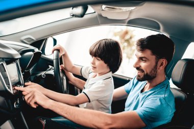 Erkek çocuk ile yeni araç direksiyon başında oturuyor. Aile gülümseyerek. Otomobil bir galeride satın. Otomobil Salon. Neşeli sürücü. Mutlu birlikte. Baba ve oğul. İyi bir ruh hali. Büyük ticaret.
