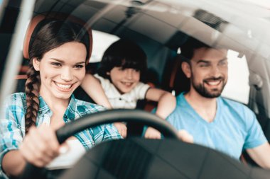 Bir kadın yeni bir araç direksiyon başında oturuyor. Aile gülümseyerek. Otomobil bir galeride satın. Otomobil Salon. Neşeli sürücü. Mutlu birlikte. Başarılı satın alma. İyi bir ruh hali. Büyük ticaret.