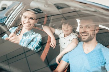 Bir kadın yeni bir araç direksiyon başında oturuyor. Genç aile. Otomobil bir galeride satın. Otomobil Salon. Neşeli sürücü. Mutlu birlikte. Başarılı satın alma. İyi bir ruh hali. Çocuk arka koltuk üzerinde.