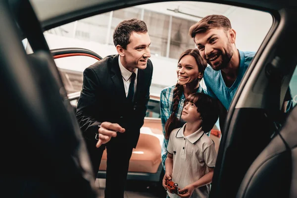 幸せな若い家族は ショールームに新しい自動車を選んでいます ディーラーとの対話 陽気なお客様 車の中に見えます 決定を下します 契約の終了です 良い提供しています 買い手と売り手 ビジネス貿易 — ストック写真