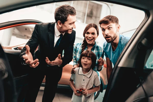 幸せな若い家族は ショールームに新しい自動車を選んでいます ディーラーとの対話 陽気なお客様 車の中に見えます 決定を下します 契約の終了です 良い提供しています 買い手と売り手 ビジネス貿易 — ストック写真