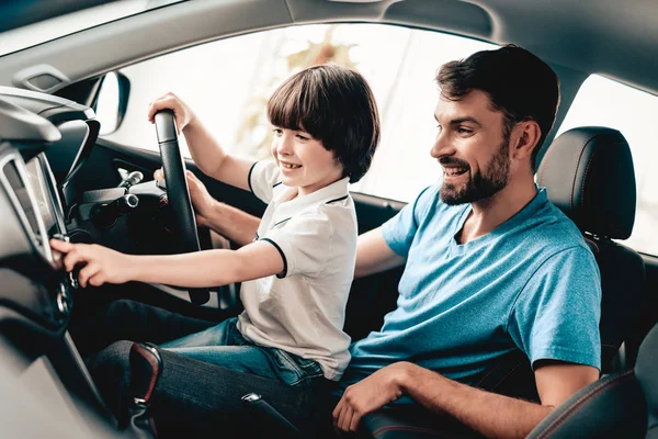 有孩子的人坐在新车的轮子上 微笑的家庭 在展厅购买汽车 汽车沙龙 开朗的司机 快乐在一起 父亲和儿子 好心情 伟大的贸易 — 图库照片