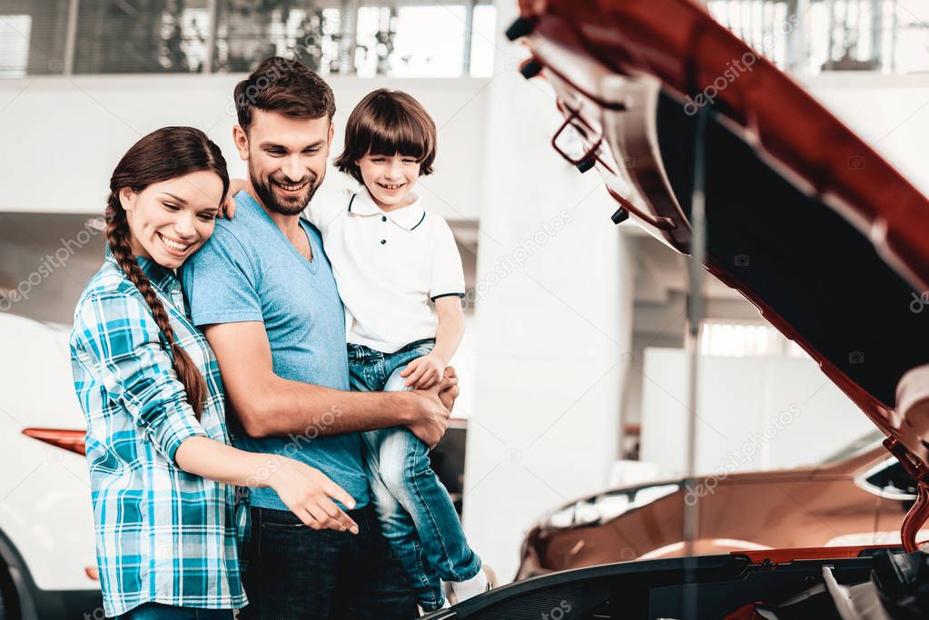 Young Family Are Choosing A New Car In Showroom. Automobile Salon. Happy Together. Good Mood. Make A Desicion. Auto Rewiew. Quality Control. Reliability Mark. Looking Under The Hood.