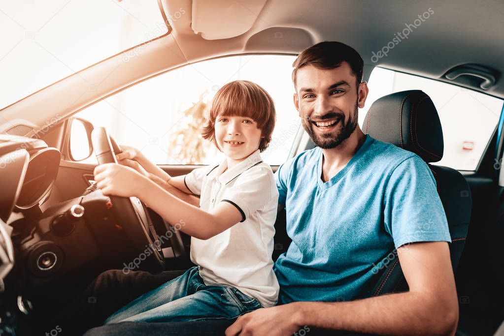 Man With Kid Are Sitting At The Wheel Of New Vehicle. Smiling Family. Car Buying In A Showroom. Automobile Salon. Cheerful Driver. Happy Together. Father And Son. Good Mood. Great Trade.