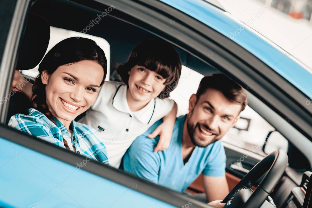 A Woman Is Sitting At The Wheel Of A New Vehicle. Smiling Family. Car Buying In A Showroom. Automobile Salon. Cheerful Driver. Happy Together. Successful Buying. Good Mood. Great Trade.