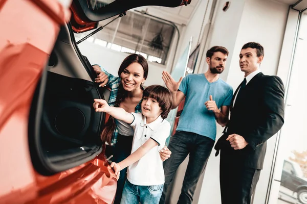 快乐的年轻家庭正在选择一个新的汽车在展厅 与经销商对话 愉快的客户 看看后备箱里面作出决定 很好的报价 买方和卖方 商业贸易 — 图库照片