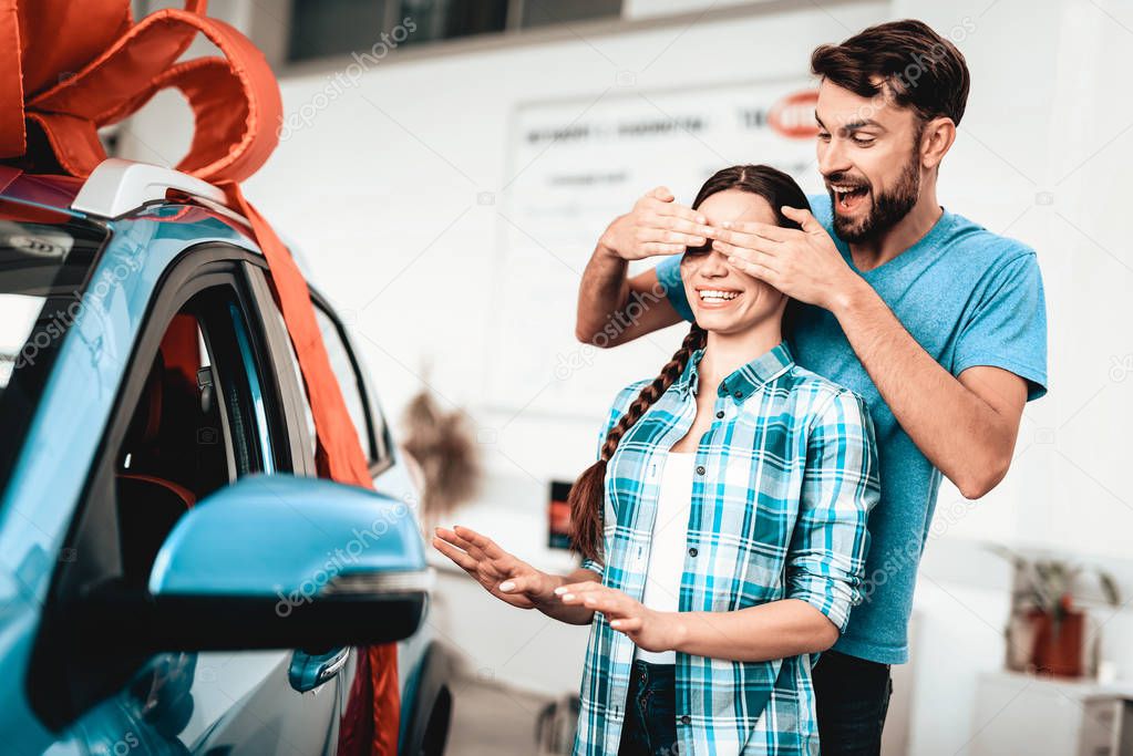 A Guy Shows A New Car To Girlfriend. Present Concept. Staring At Each Other. Automobile Salon. Make A Decision. Gift Ribbon. Eyes Closed. Good Offer. Happy Together. Successful Buying.