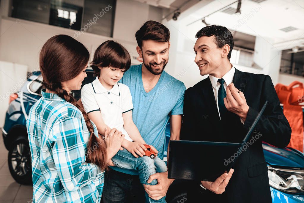 Happy Young Family Are Choosing A New Car In Showroom. Dialogue With Dealer. Cheerful Customer. Automobile Salon. Make A Decision. Information On Tablet. Good Offer. Buyer And Seller. Business Trade.