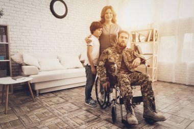 Male Veteran In Wheelchair Homecoming Concept. Home Meeting. Son And Wife. Embrace With Family. Camouflage Uniform. Child Hanging. Heroic Comeback. Paralyzed Soldier. Disabled Man. clipart